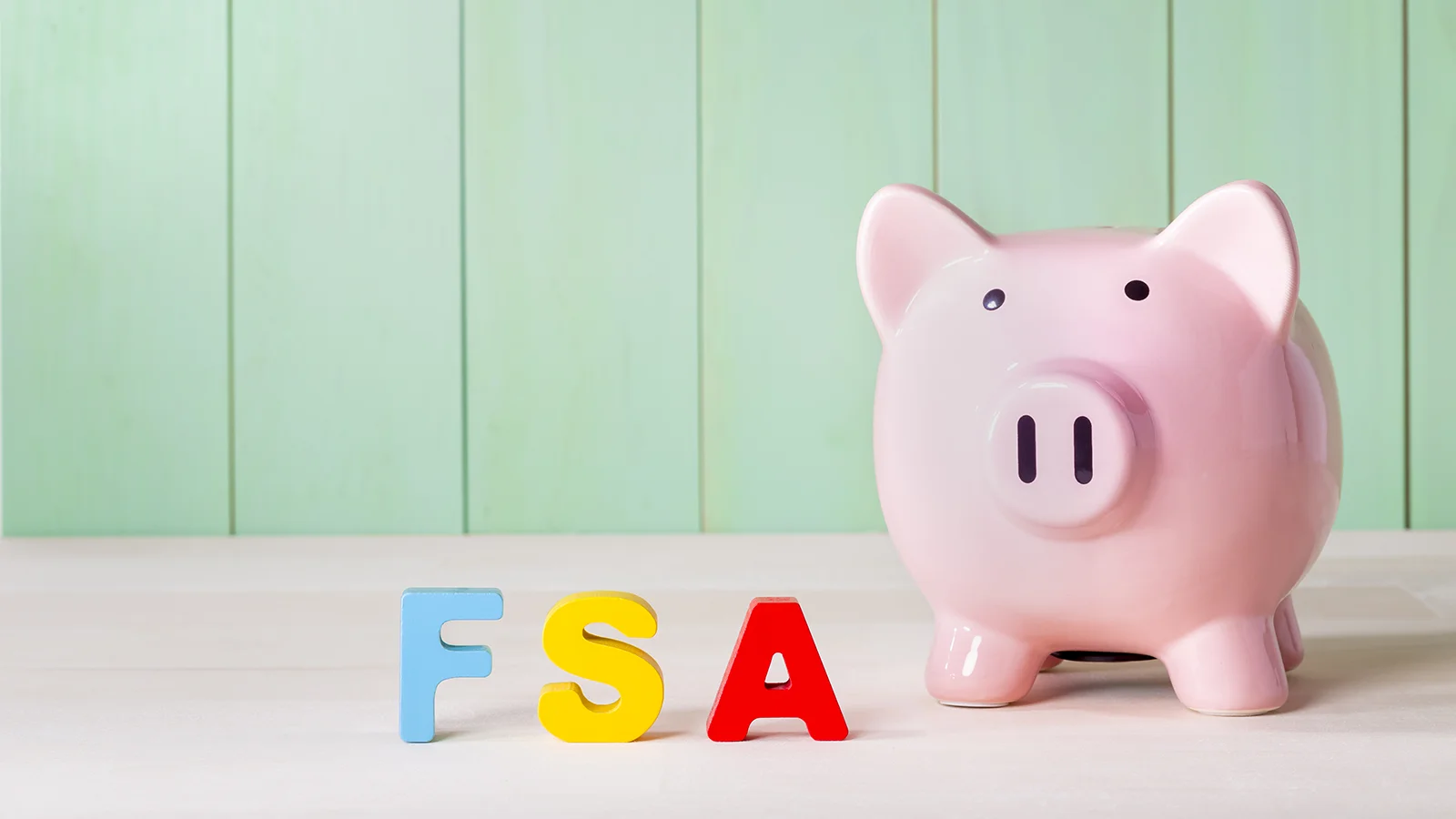 pink piggy bank on table with block letters spelling out "FSA"